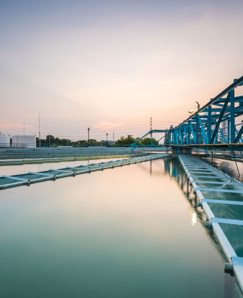 Large water treatment facility with blue structures and calm water at sunset